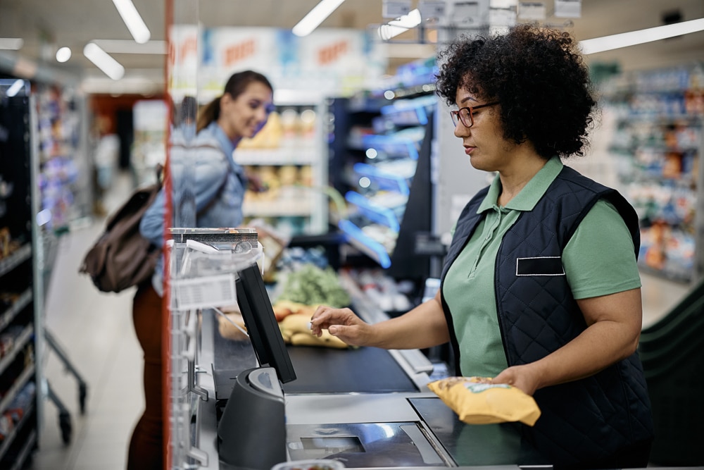 Supermarket cashier scanning customer's groceries at checkout.