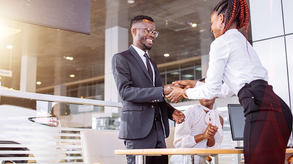 Smiling car buyer shakes the hand of a salesperson, receiving keys.