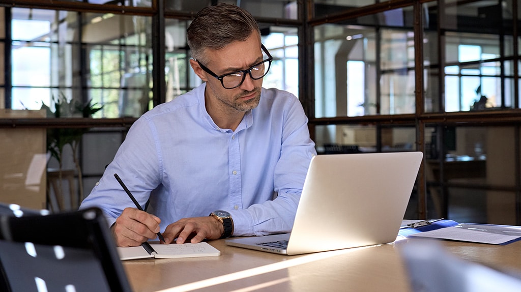 A business owner writes out his strategy on a notepad while reading laptop.
