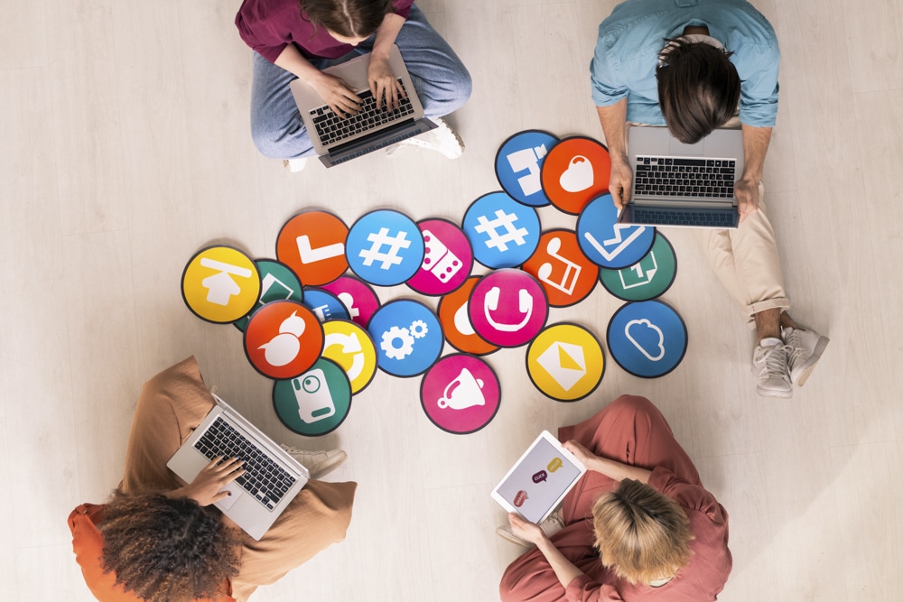 Young friendly people in casualwear sitting by multi-color papers with icons